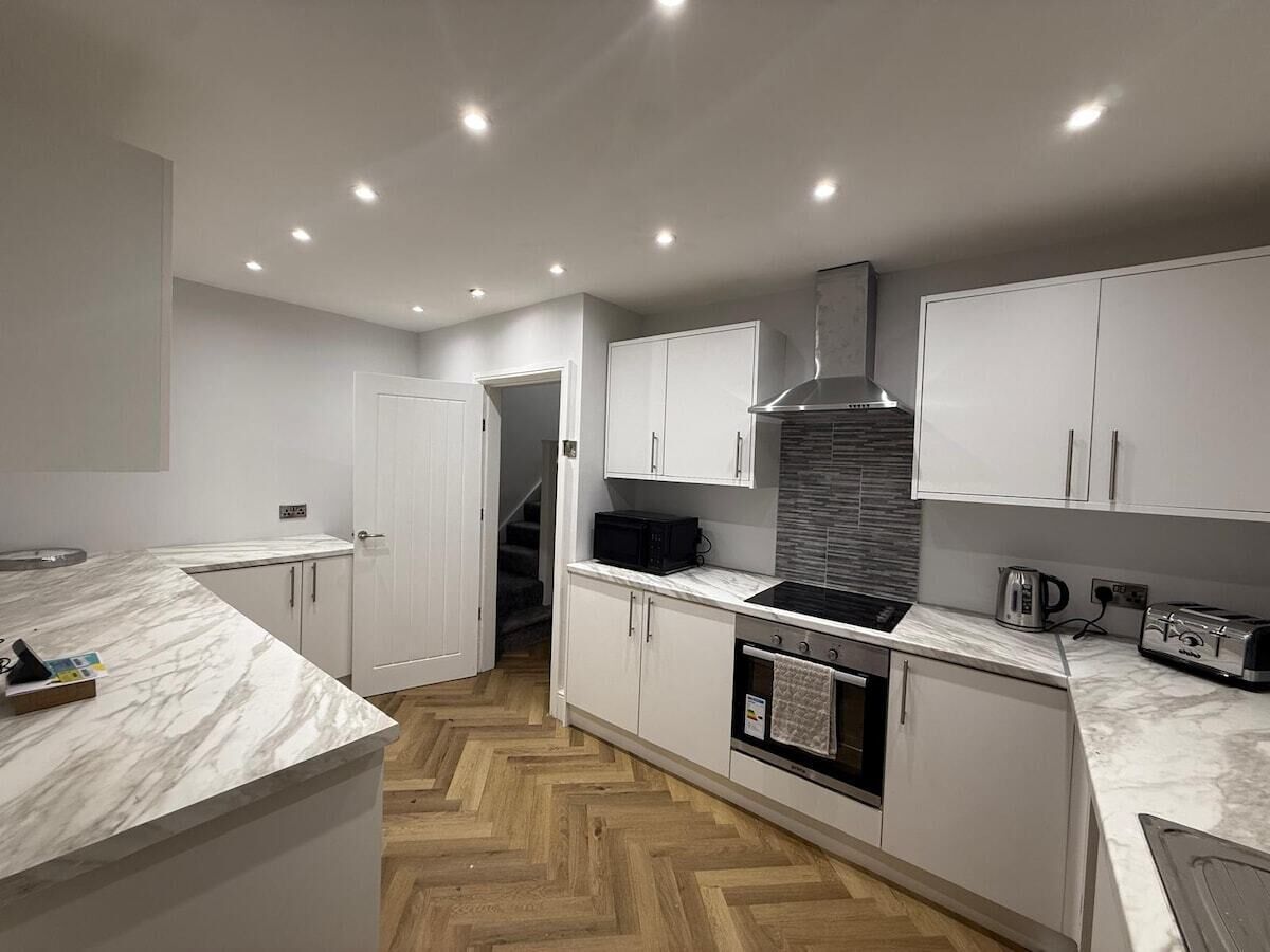 A modern kitchen with white cabinetry, a marble countertop, a built-in oven, and a stainless steel range hood.