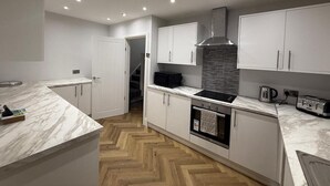 A modern kitchen with white cabinetry, a marble countertop, a built-in oven, and a stainless steel range hood.