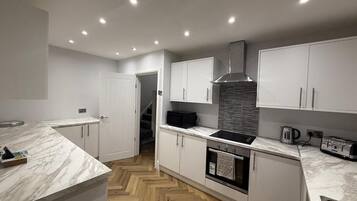 A modern kitchen with white cabinetry, a marble countertop, a built-in oven, and a stainless steel range hood.
