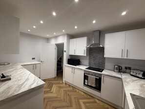A modern kitchen with white cabinetry, a marble countertop, a built-in oven, and a stainless steel range hood.