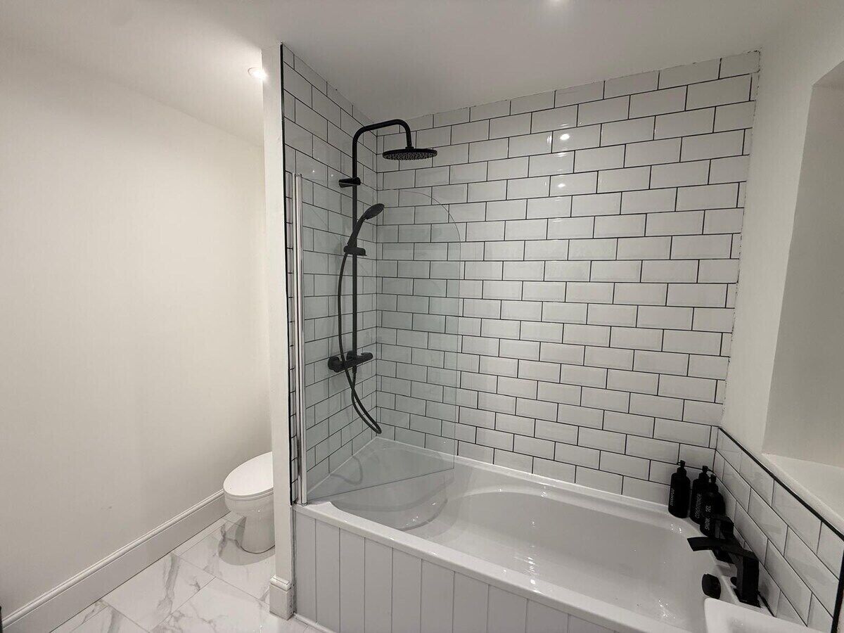 A modern bathroom with a glass-enclosed shower, white subway tiles, a white bathtub, and a toilet.