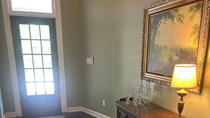 A hallway with a patterned rug, a wooden cabinet with glassware, and a framed painting on the wall. - The Parlor at Big Red 1903, Charming historic home in historic Dtown Wilmington (Wilmington)