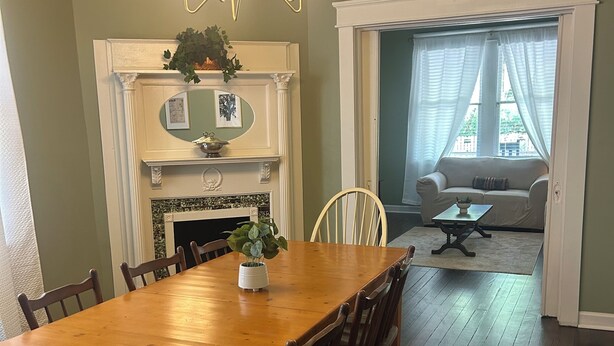 A dining room with a wooden table, chairs, a chandelier, a fireplace, and a view through a doorway. - The Parlor at Big Red 1903, Charming historic home in historic Dtown Wilmington (Wilmington)
