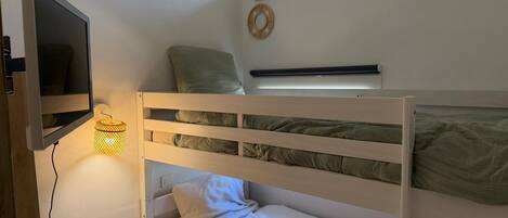Uma cama de solteiro com uma televisão fixada na parede, uma janela com vista e uma mesinha com abajur.