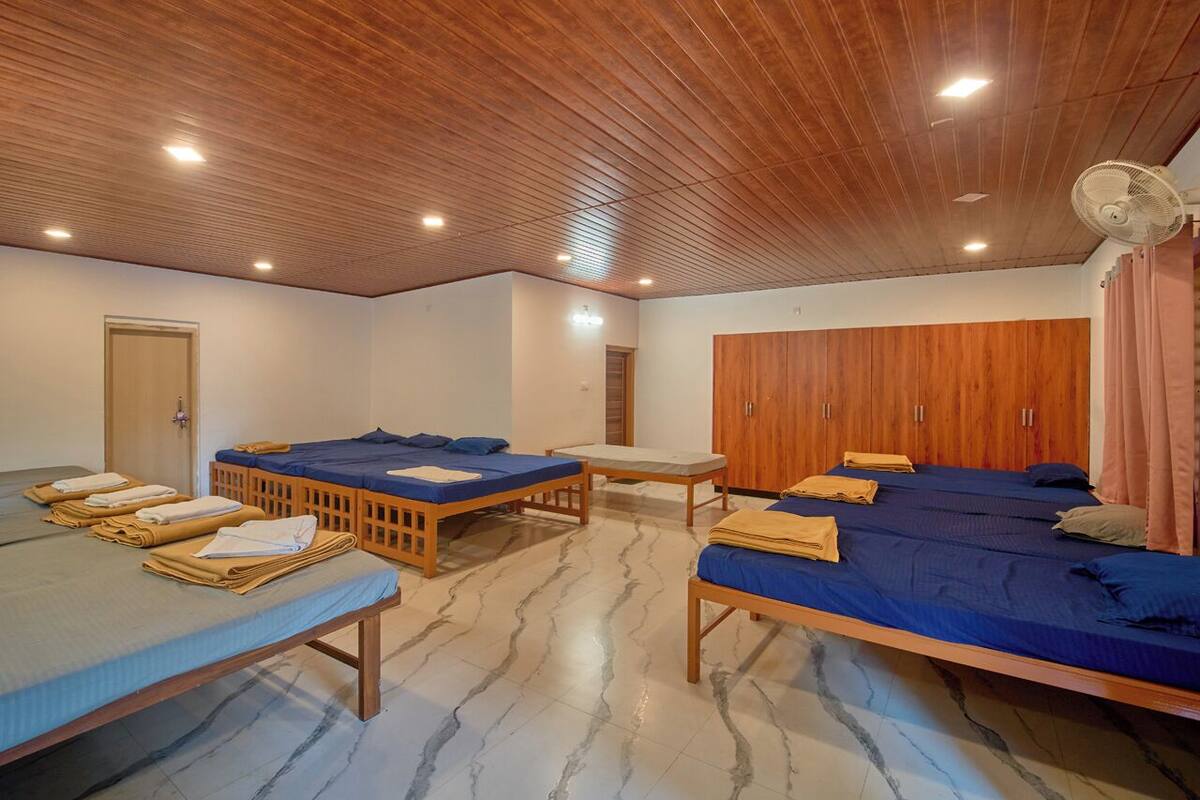 A room with four single beds, wooden furniture, a wardrobe, and a fan.