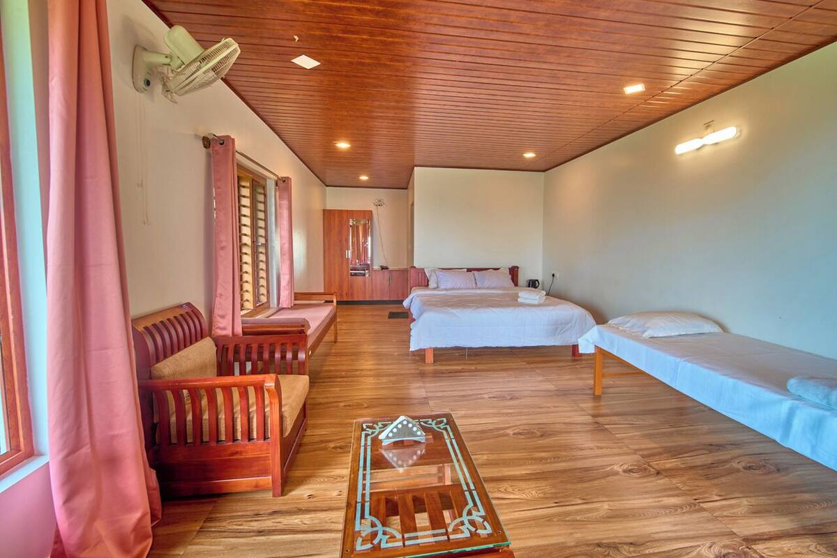 A room with wooden flooring, a bed, a sofa, a table, and a ceiling fan.