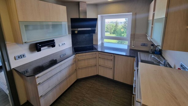A modern kitchen with wooden cabinets, a black countertop, and a window with a view of greenery. - Just like home, D3 OG? (Kreßberg)