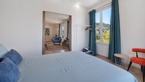 Ein Schlafzimmer mit einem großen Bett, einem Sessel, einem kleinen runden Tisch und Blick ins Freie durch ein Fenster.