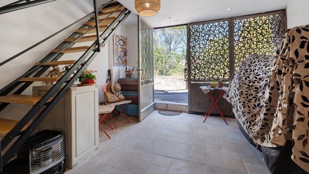 Eine Treppe mit modernem Design, ein großes Fenster mit Blick auf Grünflächen und ein Bett mit einem blattgemusterten Überwurf.