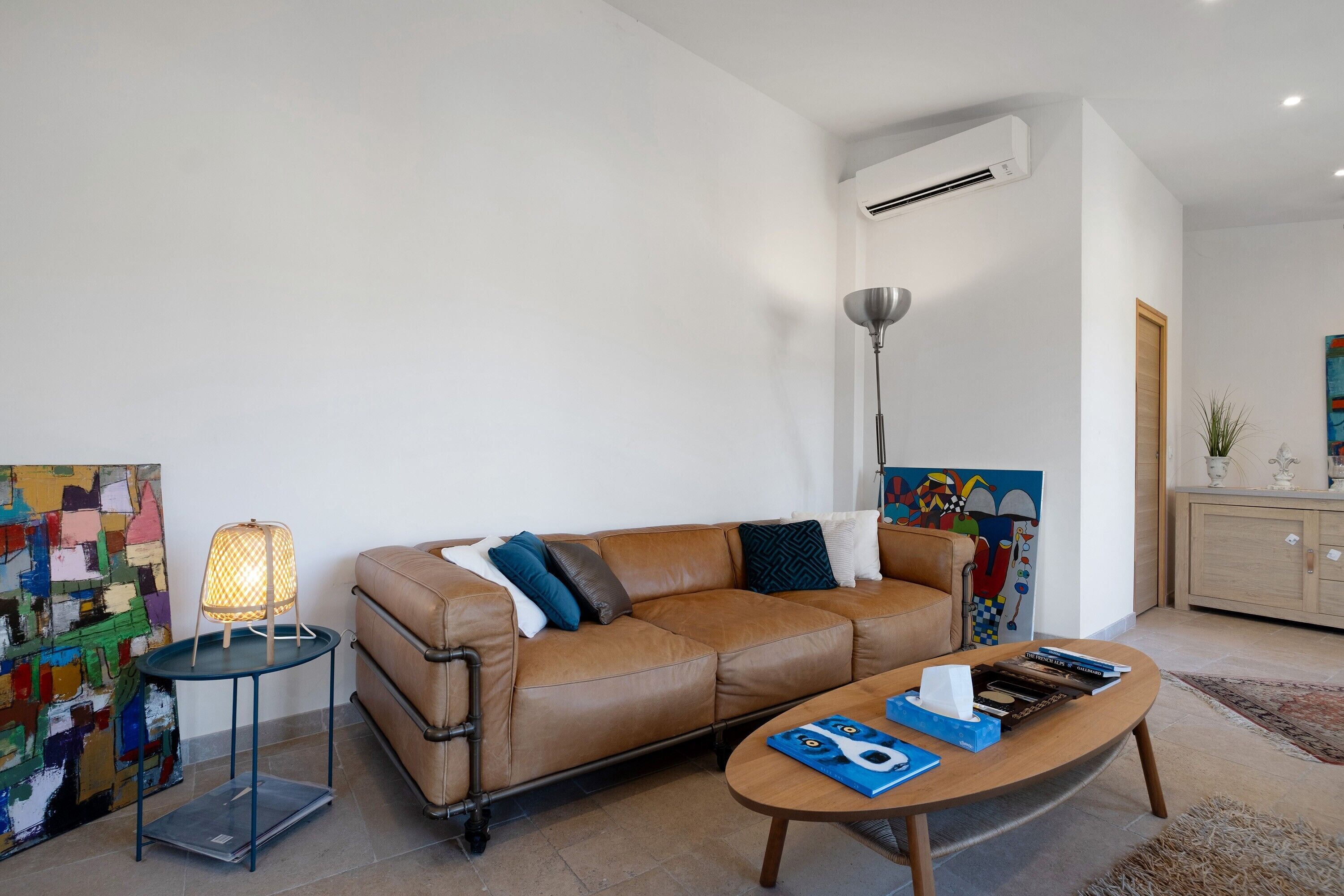 Un salon moderne avec un canapé en cuir, une table basse, un lampadaire et des œuvres d’art accrochées aux murs.