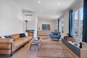 Ein modernes Wohnzimmer mit einem Ledersofa, einem blauen Sessel, einem Couchtisch und einer Kommode mit Dekorationselementen.