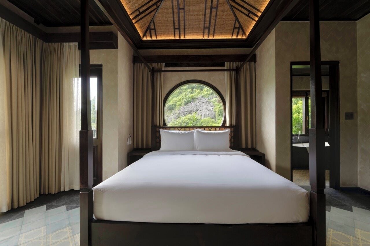Ein Schlafzimmer mit einem großen Bett, einem Rundfenster und Blick ins Grüne.