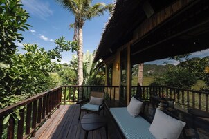 A wooden deck with outdoor seating, surrounded by lush greenery and a clear sky.