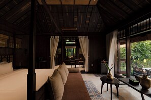 A room with a bed, a sofa, a dining table, and a view of greenery outside.