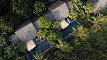 Vista aérea de un complejo turístico con varias cabañas sobre el agua, una piscina central y exuberante vegetación tropical.