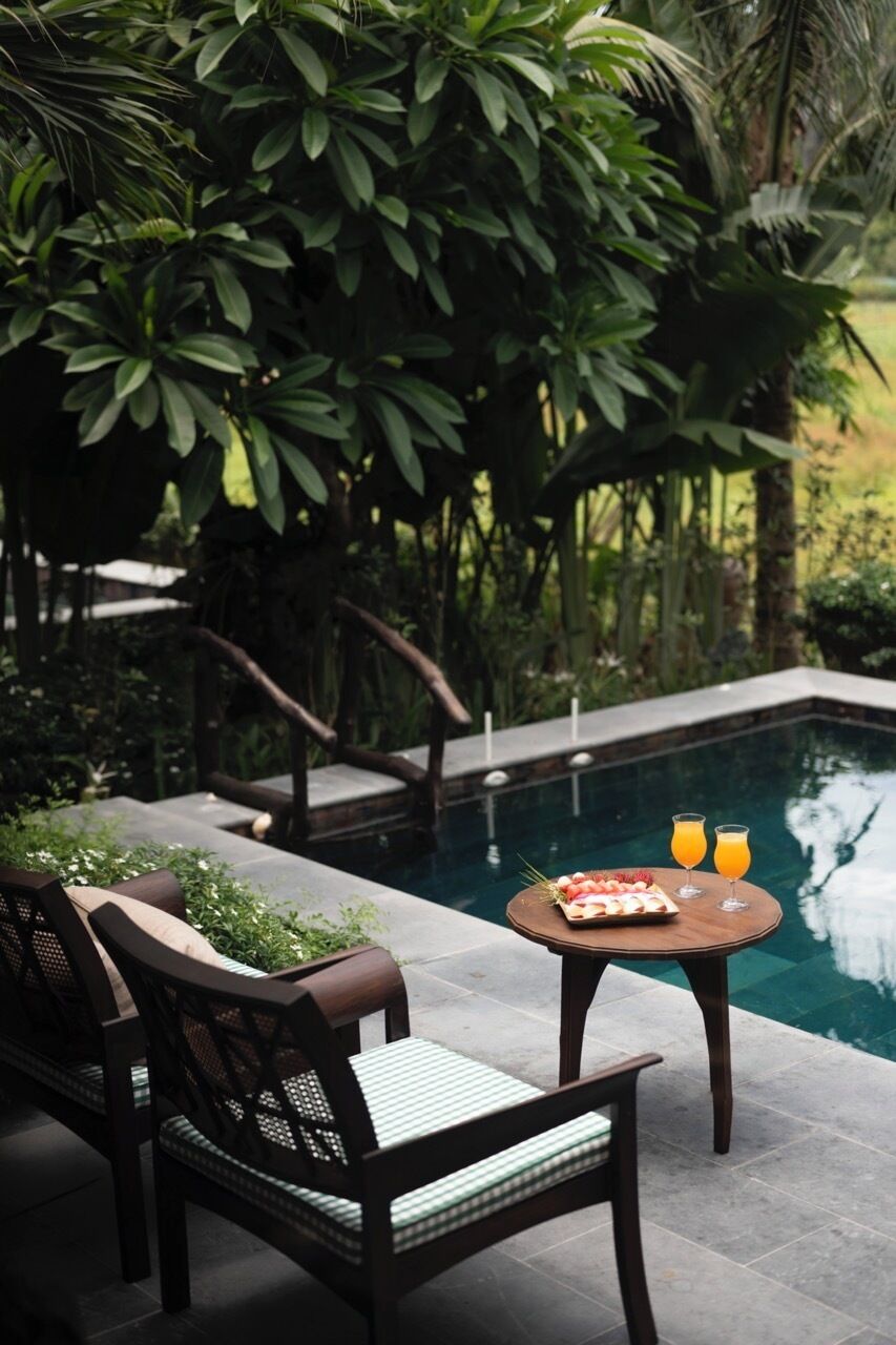 Zona junto a la piscina con una mesa para dos, rodeada de exuberante vegetación.