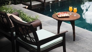 Zona junto a la piscina con una mesa para dos, rodeada de exuberante vegetación.