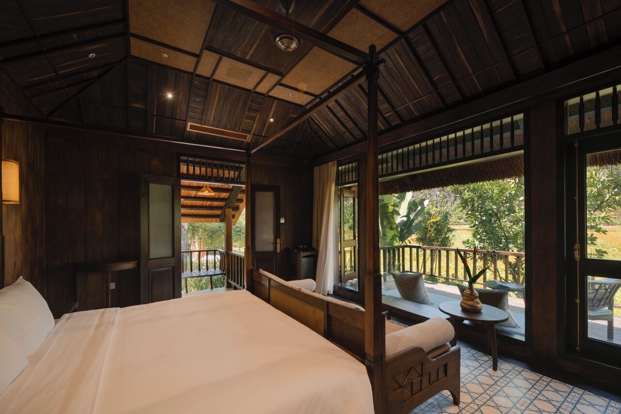 A room with a four-poster bed, a balcony with a table and chairs, and large windows.
