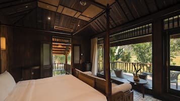 A room with a four-poster bed, a balcony with a table and chairs, and large windows.