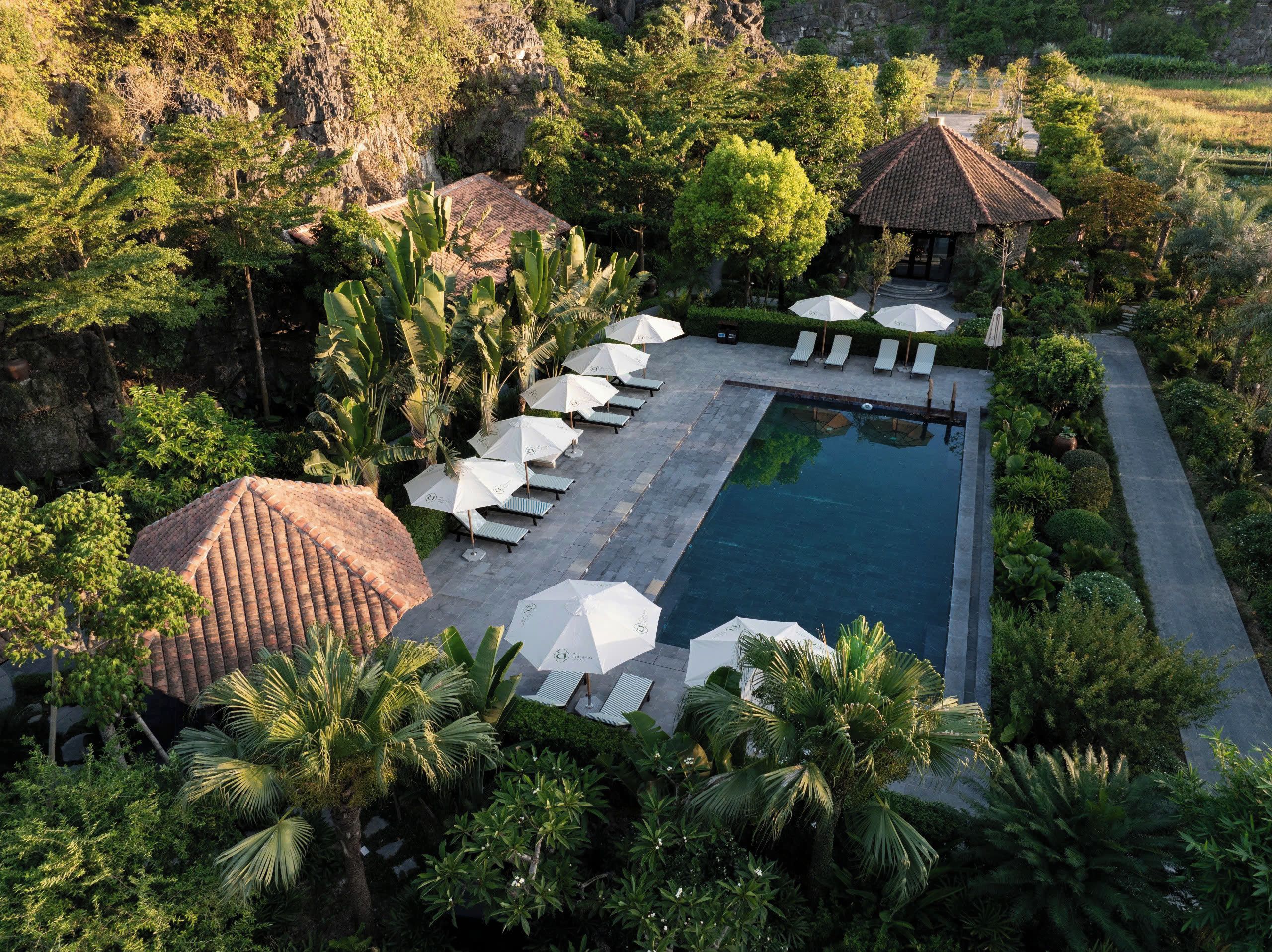 Un espace piscine agrémenté de chaises longues et de parasols, entouré d’une végétation luxuriante et d’un paysage rocheux.