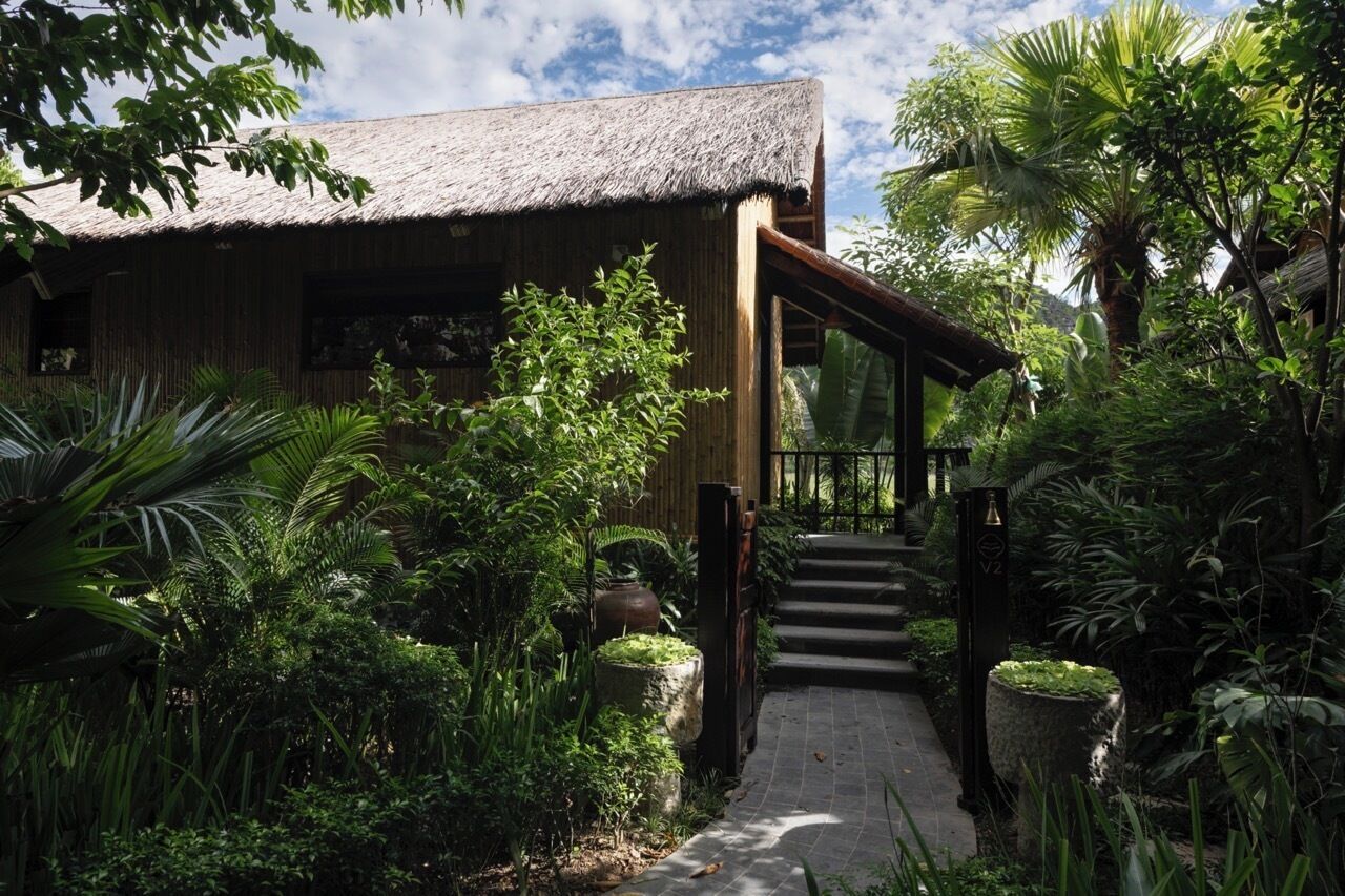 A rustic building with a thatched roof, surrounded by lush greenery and a stone pathway leading to the entrance.