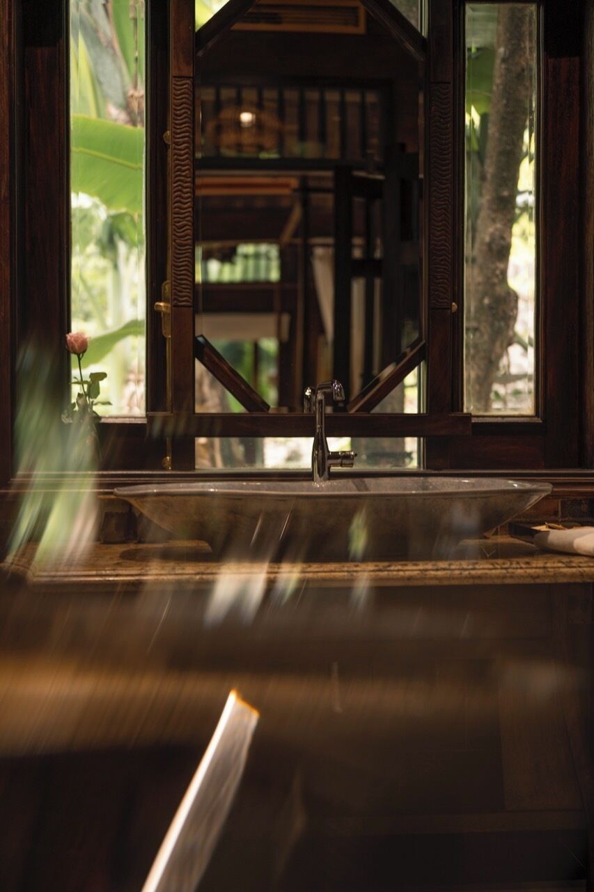 A view through a window with a wooden frame, a sink, and a rose in a vase.