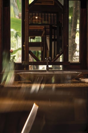 A view through a window with a wooden frame, a sink, and a rose in a vase.