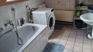 Ein kleines, helles Bad im Dachgeschoss mit einer Waschmaschine, einer Badewanne und einem Waschbecken.