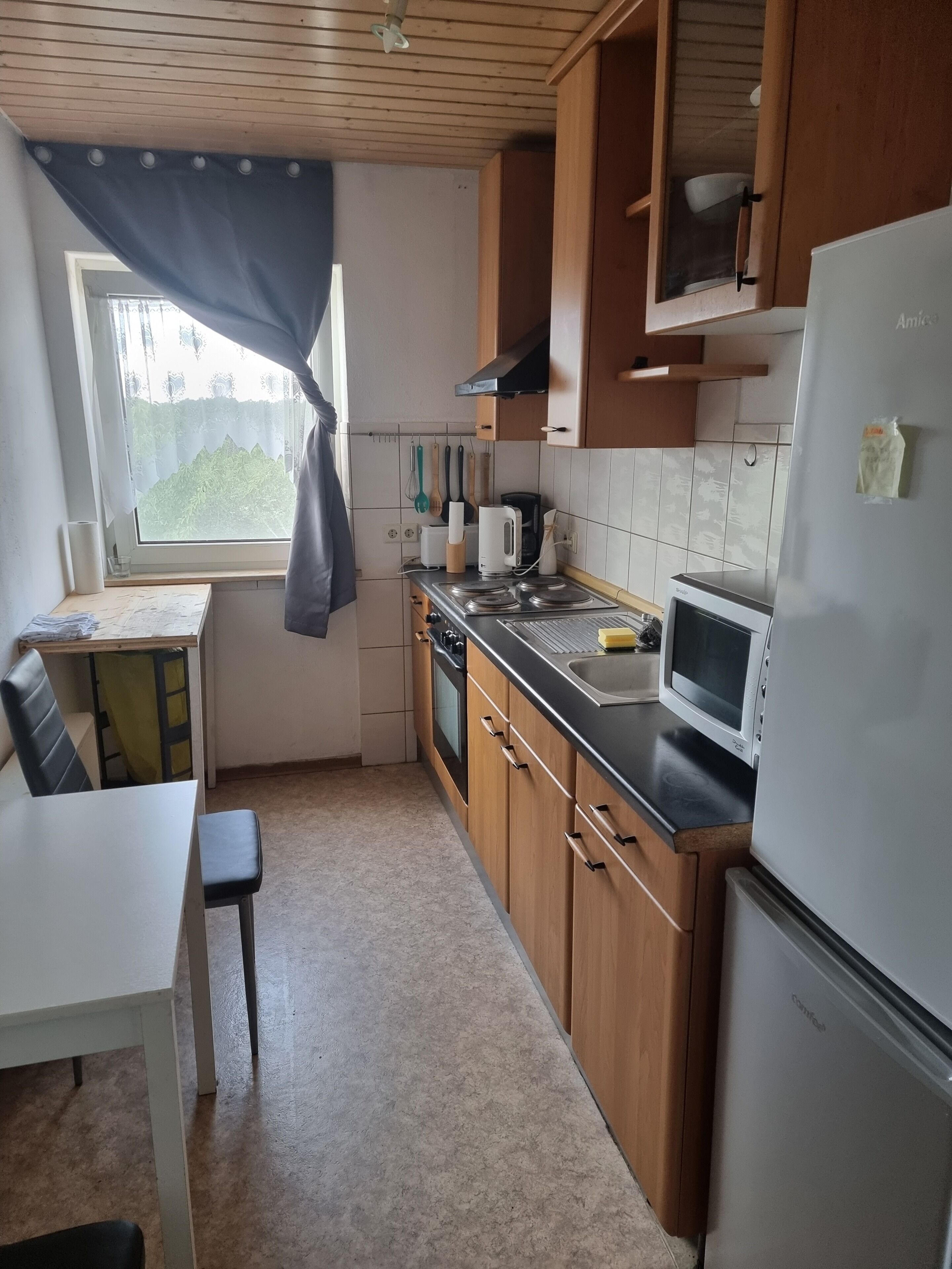 Eine kompakte Küche mit Holzausbau, einer Mikrowelle, einem Herd und einem Kühlschrank.