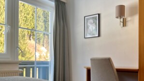 Ein Zimmer mit einem Bett, einem Schreibtisch, einem Stuhl, einem Vorhangfenster und einer Wandleuchte.
