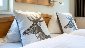 Ein Bett mit zwei Kopfkissen mit einem Hirsch-Motiv, einem Holzkopfstück und einer wandmontierten Lampe.