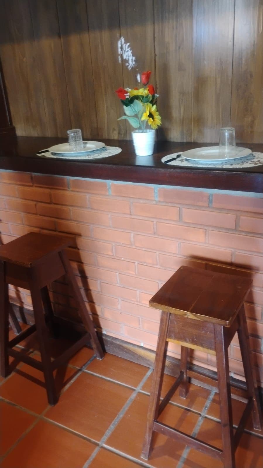 Una zona de bar con dos taburetes, una barra de madera y una pared de ladrillo.