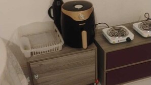 A room with a wooden cabinet, a black and gold coffee maker, a white fan, and a black kettle on a wooden table. - Chale Zafira (Tibau do Sul)