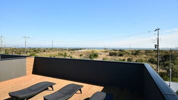 A rooftop deck with two lounge chairs, a view of the landscape, and power lines in the distance.