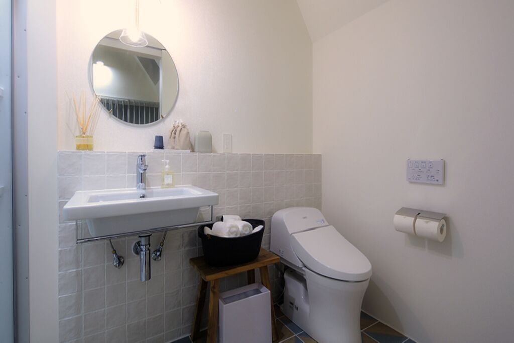 A bathroom with a sink, mirror, toilet, and a small trash bin.
