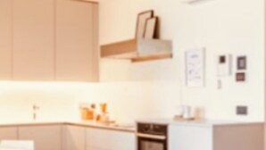 Cozinha moderna com armários brancos, forno embutido e área de refeições com mesa e cadeiras brancas.