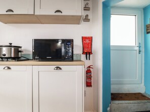 Een keuken met een magnetron, een pan op het fornuis, een branddeken en een brandblusser.