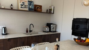Una cocina moderna con comedor, armarios blancos, una cafetera y un frutero.