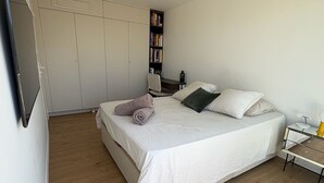 Un dormitorio con cama, mesita de noche, lámpara, estantería y una planta.