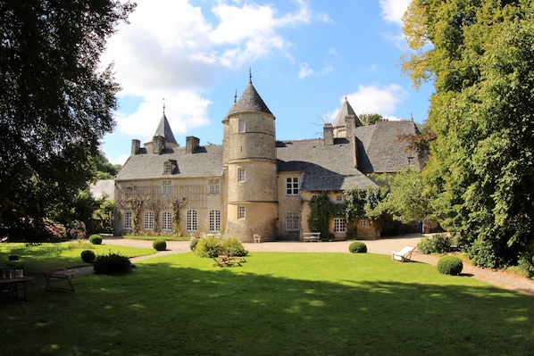 A large, historic building with multiple towers and a well-maintained garden.