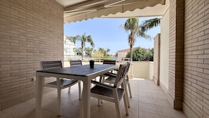 Varanda com mesa e cadeiras, um vaso com planta e vista para palmeiras e edifícios.