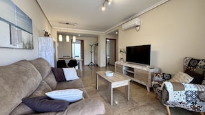 Uma sala de estar com sofá, mesa de centro, televisão e poltrona estampada.