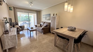Uma sala de estar com sofá, mesa de jantar e mesa de centro. Há uma janela com vista para o exterior.