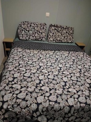 Ein Bett mit einem gemusterten Überwurf und passenden Kissen, zwei Nachttische und eine helle Wand.