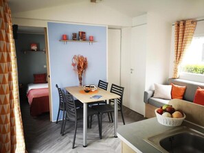 A compact living space with a dining area, kitchenette, and a sofa with cushions. - Mobile Home Near Chateau de Chaumont (Veuzain-sur-Loire)