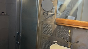 Une salle de bain dotée d’une douche à parois de verre, d’un lavabo blanc avec un robinet doré et de carreaux décoratifs sur les murs.