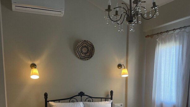Une chambre à coucher comprenant un lit, deux tables de chevet, un lustre, un climatiseur et une fenêtre avec des rideaux.
