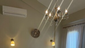 Un lit bien fait, avec du linge de lit blanc, une structure en métal noir et un coussin décoratif. On y trouve également un climatiseur mural, un lustre et une table de chevet avec une lampe.