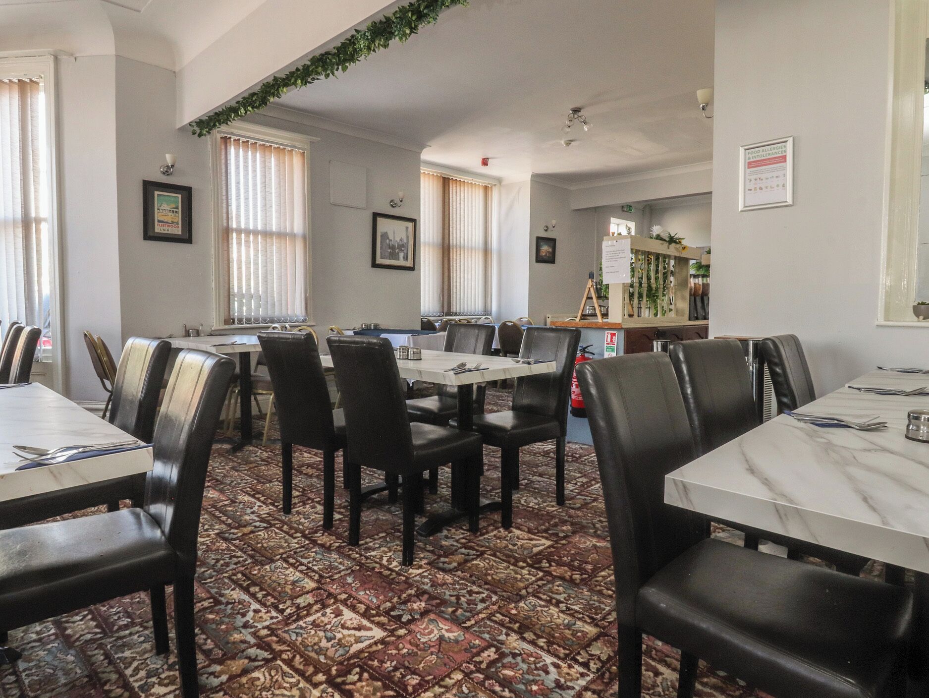A dining area with tables and chairs, a patterned carpet, and framed pictures on the walls.