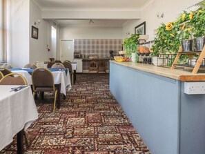 Uma área de refeições de hotel, com mesas, cadeiras, um balcão de buffet e um tapete estampado.